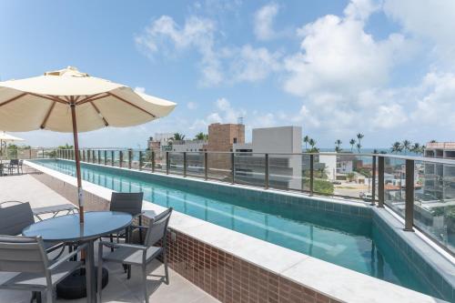 a patio with a table and umbrella and a swimming pool at Season Smart Flat Ipojuca in Porto De Galinhas