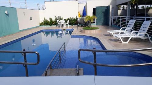 einen Pool mit weißen Stühlen neben einem Gebäude in der Unterkunft Barra prime 1539 in Barra dos Coqueiros