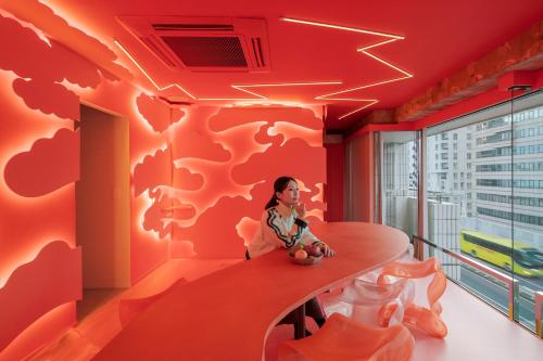 a woman sitting at a table in a room with a red wall at Art House HINODE 10 people 3 minutes from the station Art and Tokyo Bay spectacular ocean view in Tokyo