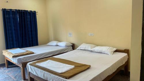 two beds in a room with blue curtains at Stone Guest House Gokarna in Gokarn