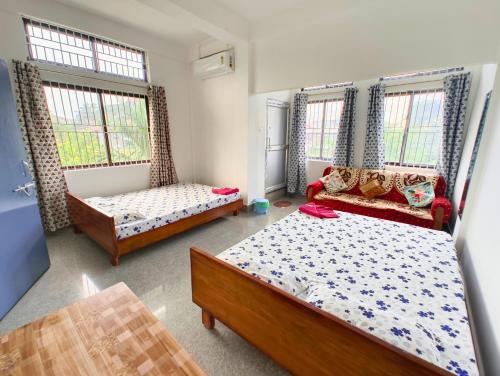 a bedroom with two beds and a couch and windows at Premium AC Rooms at Taj Heritage Hotel and Restatrant in Jorhat