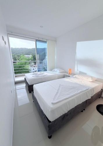 2 bedden in een witte kamer met een groot raam bij Apartamento con piscina y Aire Acondicionado en Anapoima centro in Anapoima