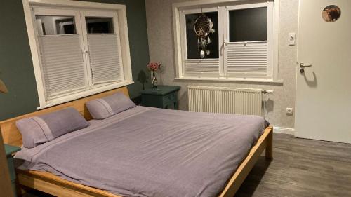 ein Schlafzimmer mit einem Bett mit violetter Bettwäsche und zwei Fenstern in der Unterkunft Waldgeflüster in Buchholz in der Nordheide