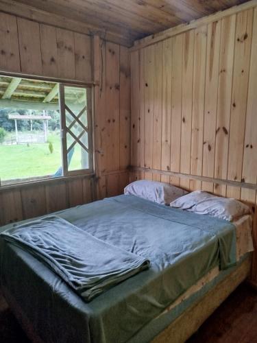 a bed in a wooden room with a window at Chácara Betel in Rancho Queimado