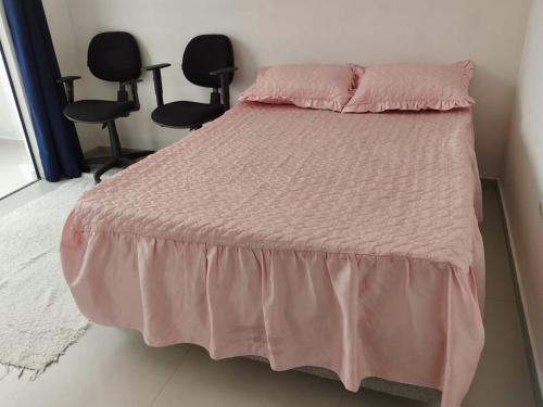 een bed met een roze dekbed en twee stoelen bij Suíte 3 Centro São Thomé das Letras in São Thomé das Letras