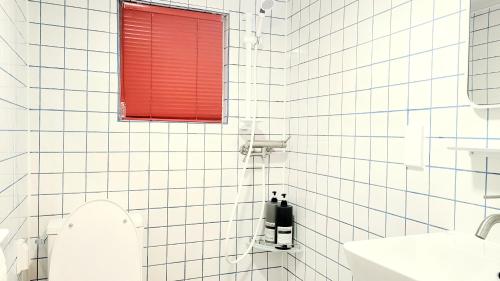 a white tiled bathroom with a red window and a toilet at Maison de Jann in Seoul