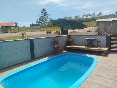 un uomo seduto sotto un ombrellone accanto alla piscina di Bella montanha pousada e camping a Lauro Müller