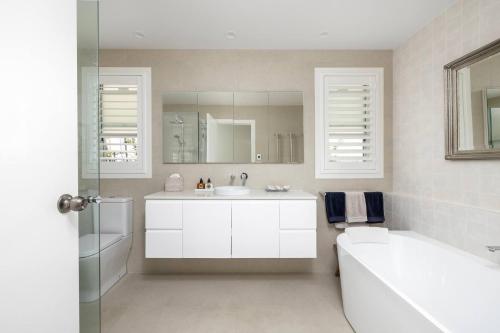 a white bathroom with a tub and a sink and a mirror at Verona in Shoal Bay