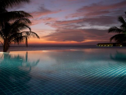 a swimming pool with palm trees and the ocean at sunset at Vilamendhoo Island Resort & Spa in Dhangethi