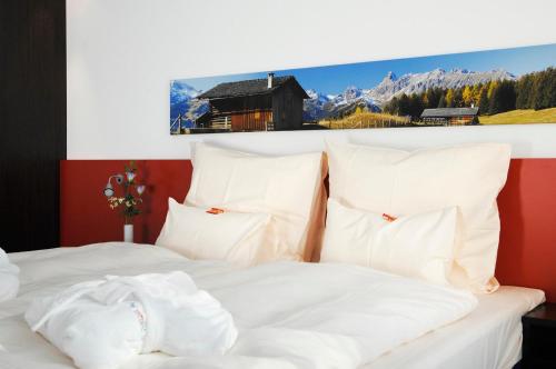 ein Bett mit weißen Kissen und einem Bild eines Berges in der Unterkunft Stay2Munich Hotel & Serviced Apartments in Brunnthal