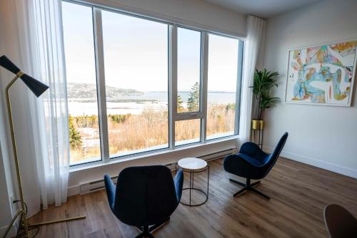 een woonkamer met 2 stoelen, een tafel en grote ramen bij 209 - Luxury Condo - Pool & River View in Baie-Saint-Paul