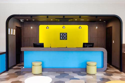 a lobby with a yellow wall and a counter with stools at KOKO HOTEL Higashiosaka - formerly Hotel Wing International Select Higashi Osaka in Osaka