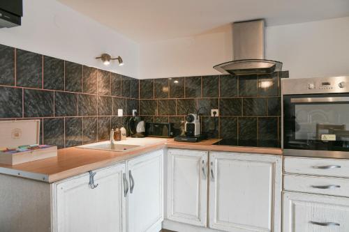 eine Küche mit weißen Schränken und einer schwarz gefliesten Wand in der Unterkunft Le Chat De Lamartine - Clim Parking in Saint-Pierre-dʼAlbigny