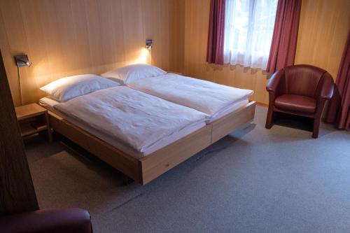 ein Schlafzimmer mit einem großen Bett und einem Stuhl in der Unterkunft Hotel Garni Alpenruh in Lenk im Simmental