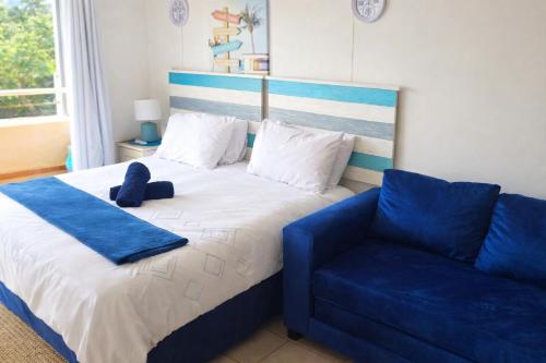 a bedroom with a bed and a blue couch at 102 L'escalier CABANAS-ON THE BEACH in Amanzimtoti
