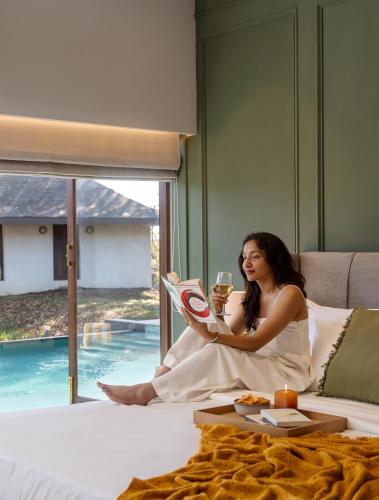 a woman sitting on a bed reading a magazine at SaffronStays La Mia Casa in Jāmb