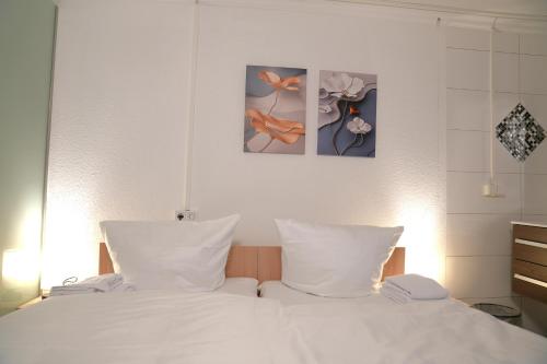 a bed with white sheets and two paintings on the wall at Hotel am Schürblick in Gronau