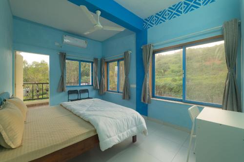 a blue bedroom with a bed and two windows at Saachi Villa in Panchgani