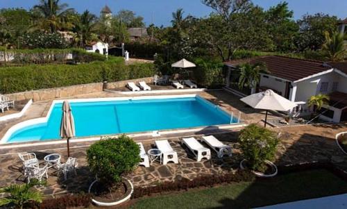 a swimming pool with chairs and umbrellas in a yard at Masai Apartments Diani in Ukunda
