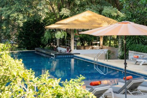 a swimming pool with an umbrella and chairs and a table at Comsaed River Kwai Resort in Kanchanaburi City