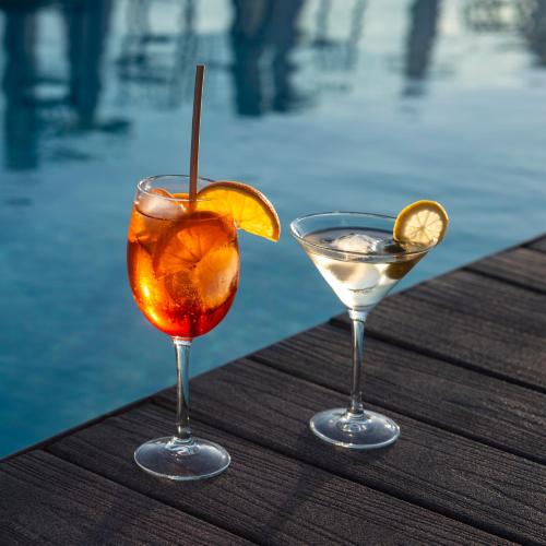 two cocktails sitting on a wooden table next to a pool at Hotel Bahía Calpe by Pierre & Vacances in Calpe