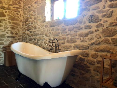 une baignoire blanche dans une salle de bains en pierre avec une fenêtre dans l'établissement Domaine du Cammazet, à Lapenne