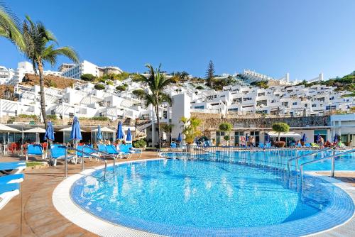 a swimming pool with blue chairs and white buildings at Bahia Blanca in Puerto Rico de Gran Canaria
