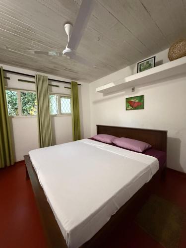 a bedroom with a large white bed and two windows at Schanigarten in Deniyaya