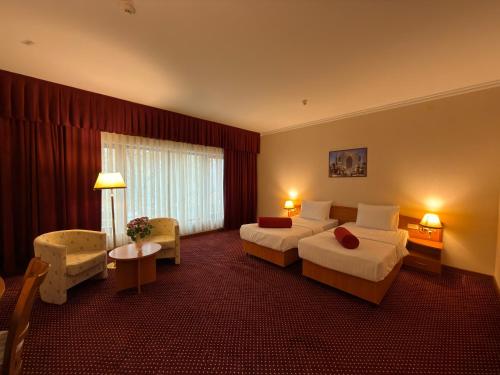 乌尔根奇Khorezm Palace Hotel的一间酒店房间，里面有两张床、一张桌子和几把椅子。