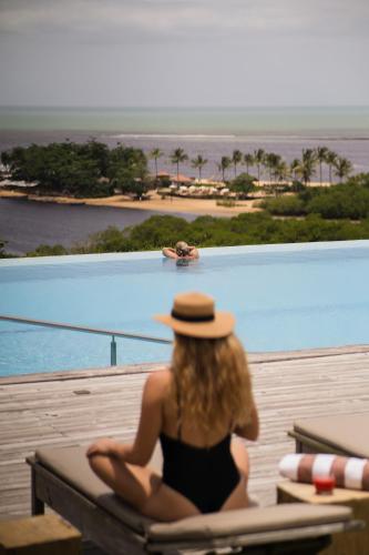 a woman in a hat sitting on a chair next to a pool at Bela Vista Hotel Boutique in Caraíva
