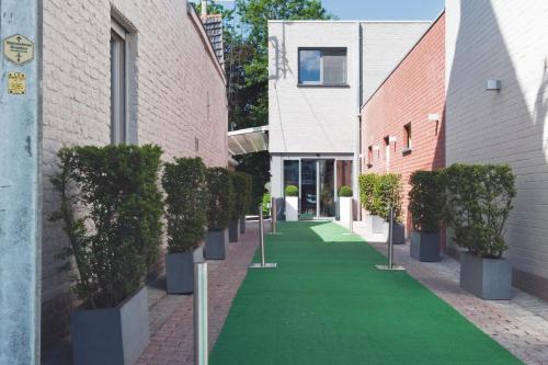 un chemin vert entre deux bâtiments avec des plantes en pot dans l'établissement Feestzaal De Kroon, à Dixmude