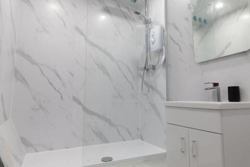 een witte badkamer met douche en wastafel bij Vacant Nests Ivy Cottage 3BR Wi-Fi in Banton