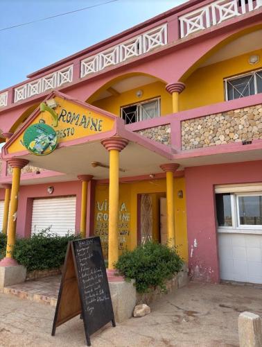 een roze en geel gebouw met een bord ervoor bij Villa Romaine in Toubab Dialaw