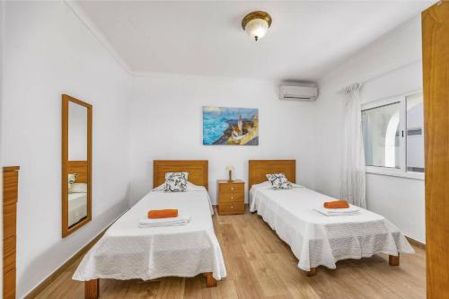 2 Betten in einem Zimmer mit weißen Wänden und Holzböden in der Unterkunft Villa Casa Alice by Villa Plus in Carvoeiro