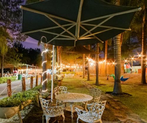a table and chairs with an umbrella and lights at Parque Girasoles Balneario & Cabañas in San Francisco del Rincón