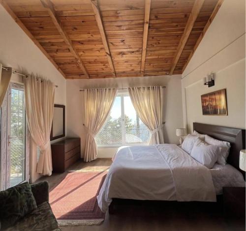 a bedroom with a large bed and windows at Haven Mushkpuri Terraces Khaira Gali - 3BR Home, Lawn, BBQ & Fireplace in Chhāngla Gali