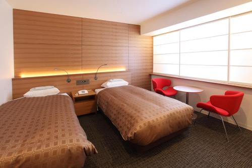 Nagaoka Grand Hotel في ناغاوكا: غرفة فندقية بسريرين وكراسي حمراء