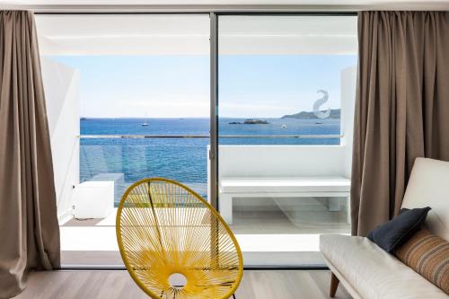ein Wohnzimmer mit einem gelben Stuhl und einem großen Fenster in der Unterkunft Sud Ibiza Suites in Ibiza-Stadt