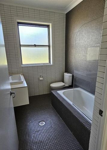 a bathroom with a toilet and a tub and a window at Beachcomber - 39 Phillip Drive South West Rocks in South West Rocks