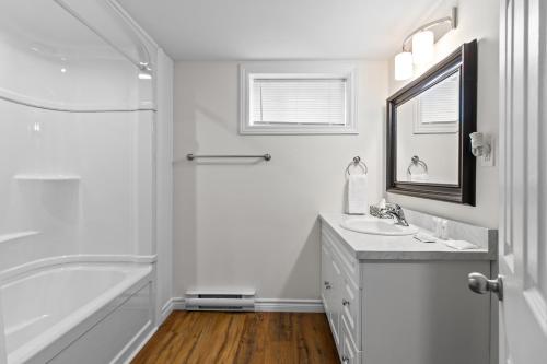 ein weißes Badezimmer mit einer Badewanne, einem Waschbecken und einem Spiegel in der Unterkunft Stylish 2BR WiFi Parking MUN Walk in St. John's