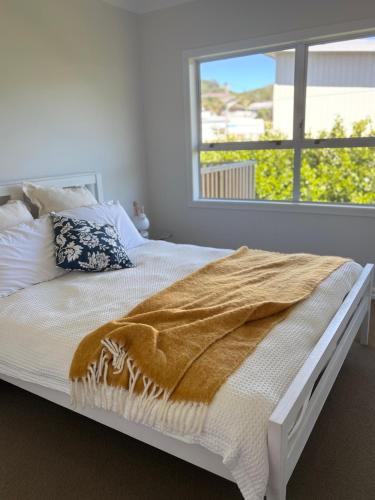 a bed with a blanket on it in a room with a window at Wee Blue Bach at Waihi Beach in Waihi Beach