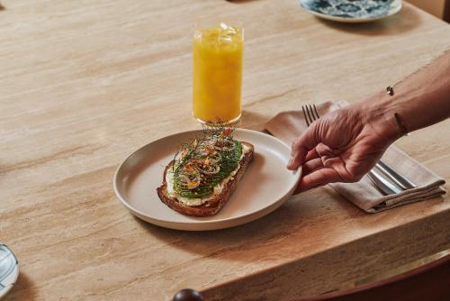 iemand die een bord vasthoudt met een sandwich en een glas sinaasappelsap bij Hyde Melbourne Place in Melbourne