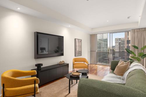 a living room with a tv and a couch and chairs at Nolo Apartments Lonsdale St in Melbourne