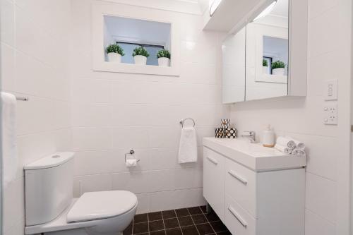 a white bathroom with a toilet and a sink at Garigal Retreat with Pool access and EV Station in Forestville