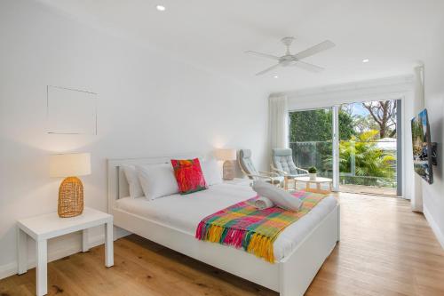 a white bedroom with a bed and a window at Garigal Retreat with Pool access and EV Station in Forestville