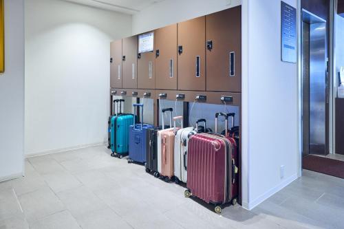 une rangée de valises alignées sur un mur dans l'établissement Hotel Lexton Kagoshima Annex, à Kagoshima
