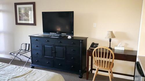 a bedroom with a black dresser with a television on it at Fair Isle Motel & The Nest in Whycocomagh