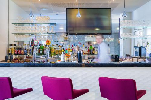 a bartender behind a bar with purple chairs at Best Western Plus Paris Velizy in Vélizy-Villacoublay