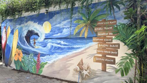 een muur met een muurschildering van een golf op het strand bij Summer of Surf Hostel Ungasan Uluwatu in Jimbaran