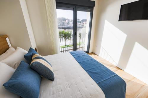 een slaapkamer met een bed met blauwe kussens en een groot raam bij Apartamentos PRAIA DO CANSORRO in Camariñas